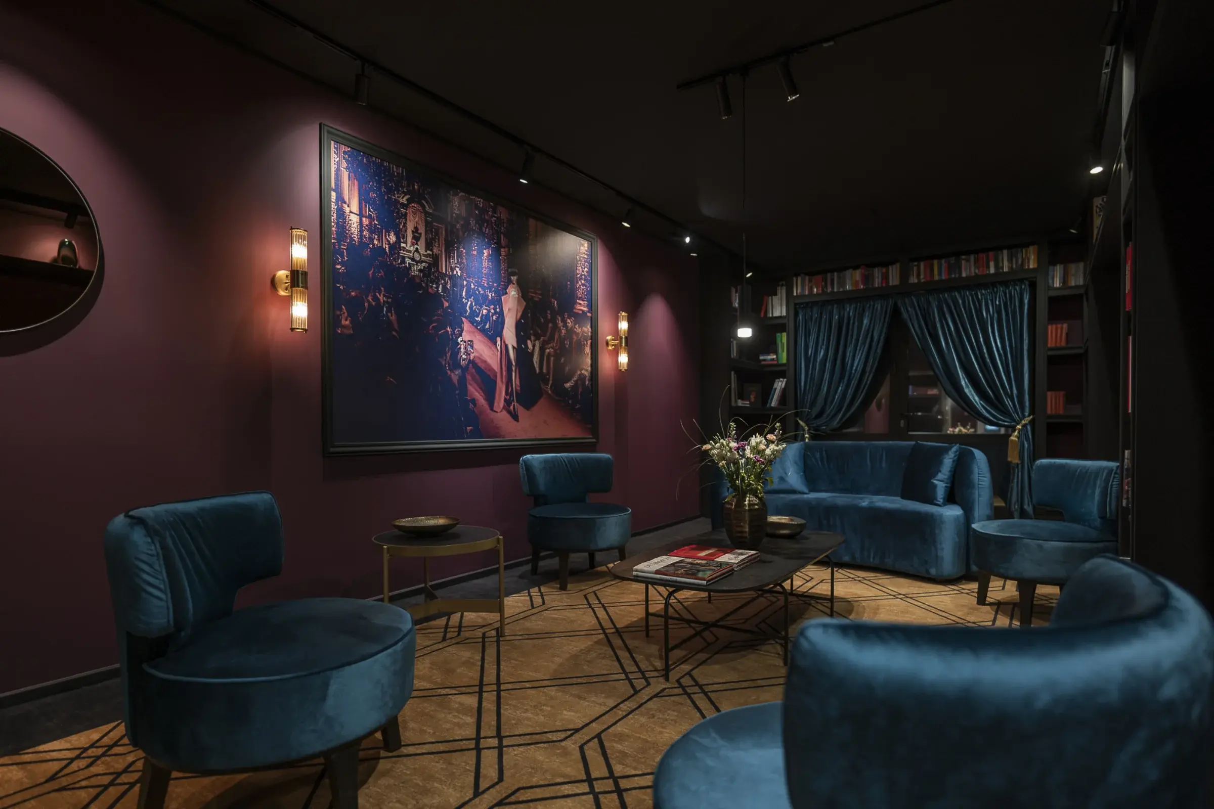 Lobby Leipzig Suites — Rückzugsort mit Bibliothek Leipzig Suites Lobby — Samtsessel, großes Kunstwerk und Bordeaux-Wand als Rückzugsort